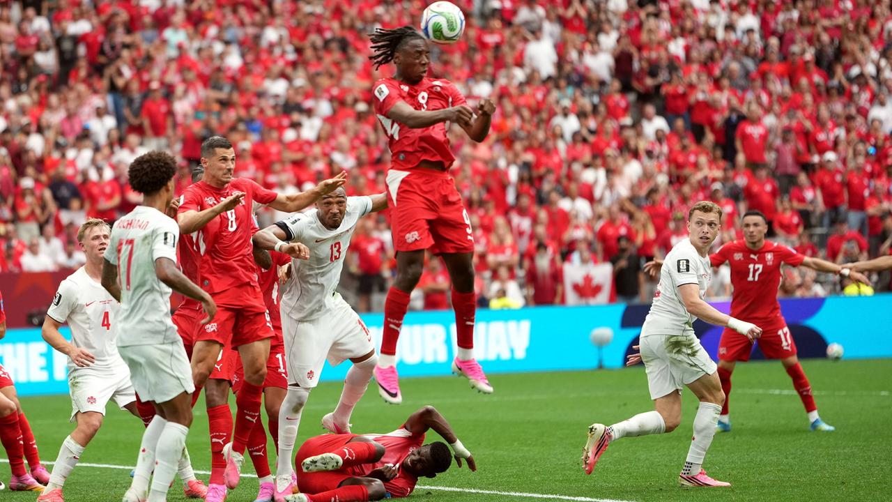 Fußball-WM: Schweiz gegen Kanada; Spieler beider Mannschaften sind auf dem Spielfeld zu sehen. Ein Schweizer Spieler springt hoch; der Ball fliegt durch die Luft.