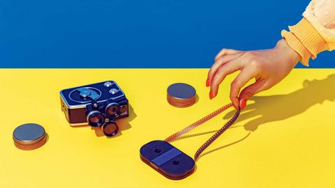 Pop Art Fotografie: Stilisiertes blau-gelbes Bild einer Retro-Kamera und einer Kassette, die eine weibliche Hand mit spitzen Fingern und lackierten Nägeln anfasst.