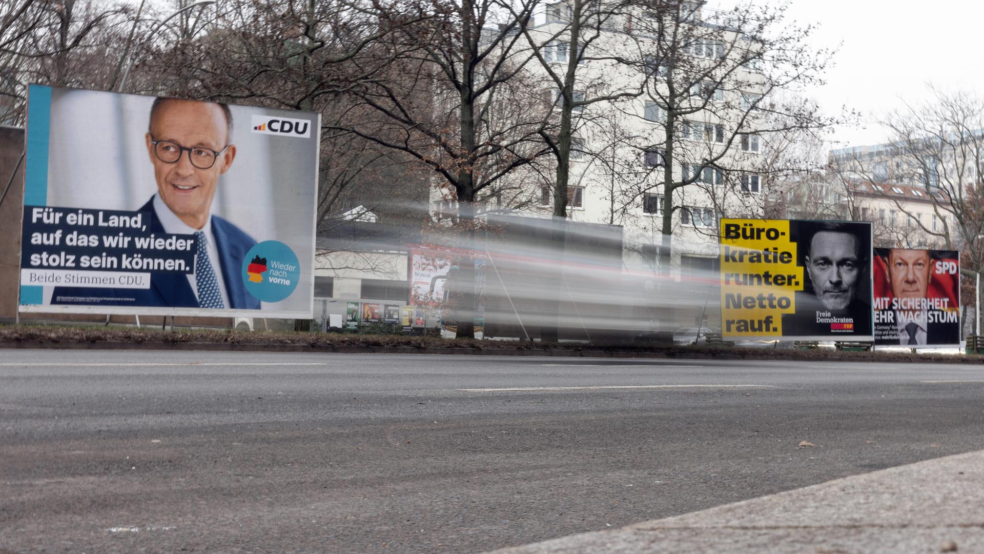 Zu sehen sind drei Wahlplakate der CDU, SPD und FDP auf einer Straße. Im Vordergrund ist ein vorüberfahrendes Auto verschwommen zu erkennen. 