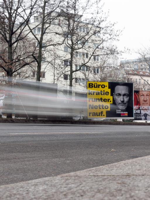 Zu sehen sind drei Wahlplakate der CDU, SPD und FDP auf einer Straße. Im Vordergrund ist ein vorüberfahrendes Auto verschwommen zu erkennen. 