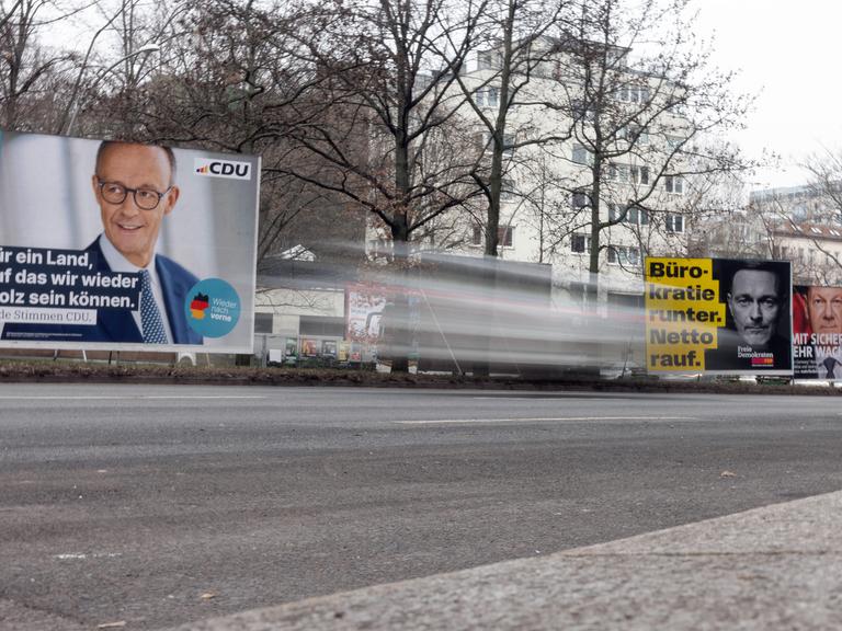 Zu sehen sind drei Wahlplakate der CDU, SPD und FDP auf einer Straße. Im Vordergrund ist ein vorüberfahrendes Auto verschwommen zu erkennen. 