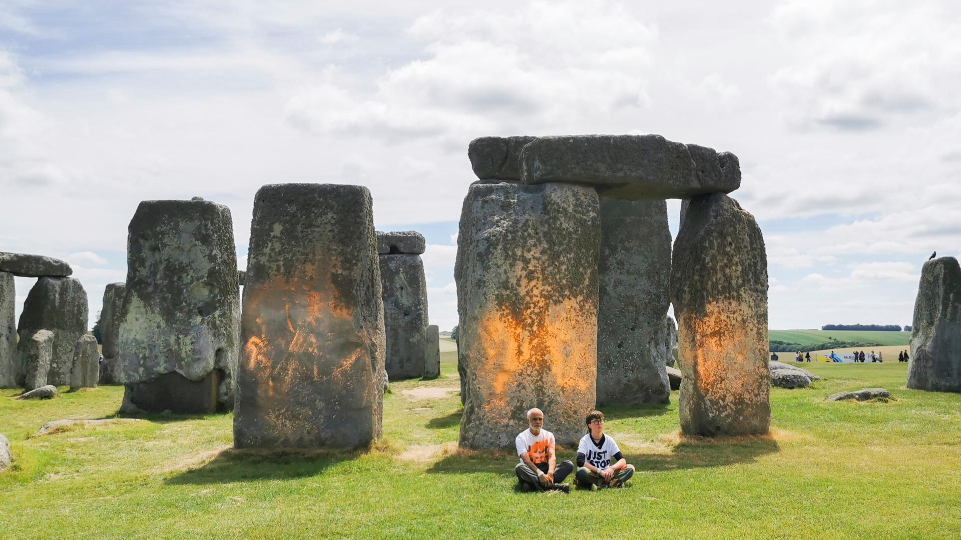 Just-Stop-Oil-Aktivisten sitzen im Gras vor dem prähistorischen Bauwerk Stonehenge in Süd-England, nachdem sie es mit oranger Farbe besprüht hatten. Just-Stop-Oil-Aktivisten sitzen im Gras vor dem prähistorischen Bauwerk Stonehenge in Süd-England, nachdem sie es mit oranger Farbe besprüht hatten.