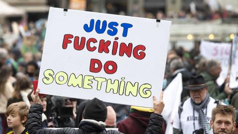 Bei einer Klimademonstration halten Demonstrierende ein Schild mit der Aufschrift "Just Fucking Do Something" hoch