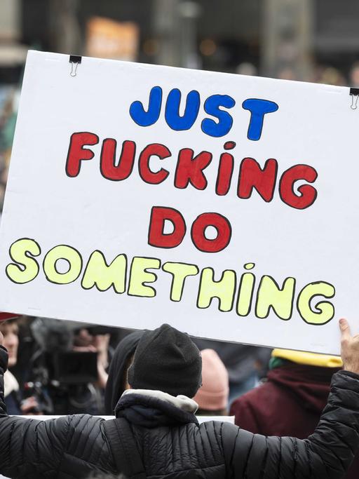 Bei einer Klimademonstration halten Demonstrierende ein Schild mit der Aufschrift "Just Fucking Do Something" hoch