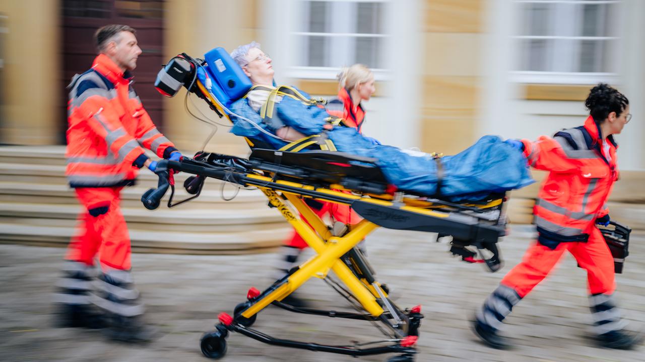 Sanitäter im Rettungseinsatz - sie schieben und ziehen eine Trage, auf der eine grauhaarige Person liegt. 