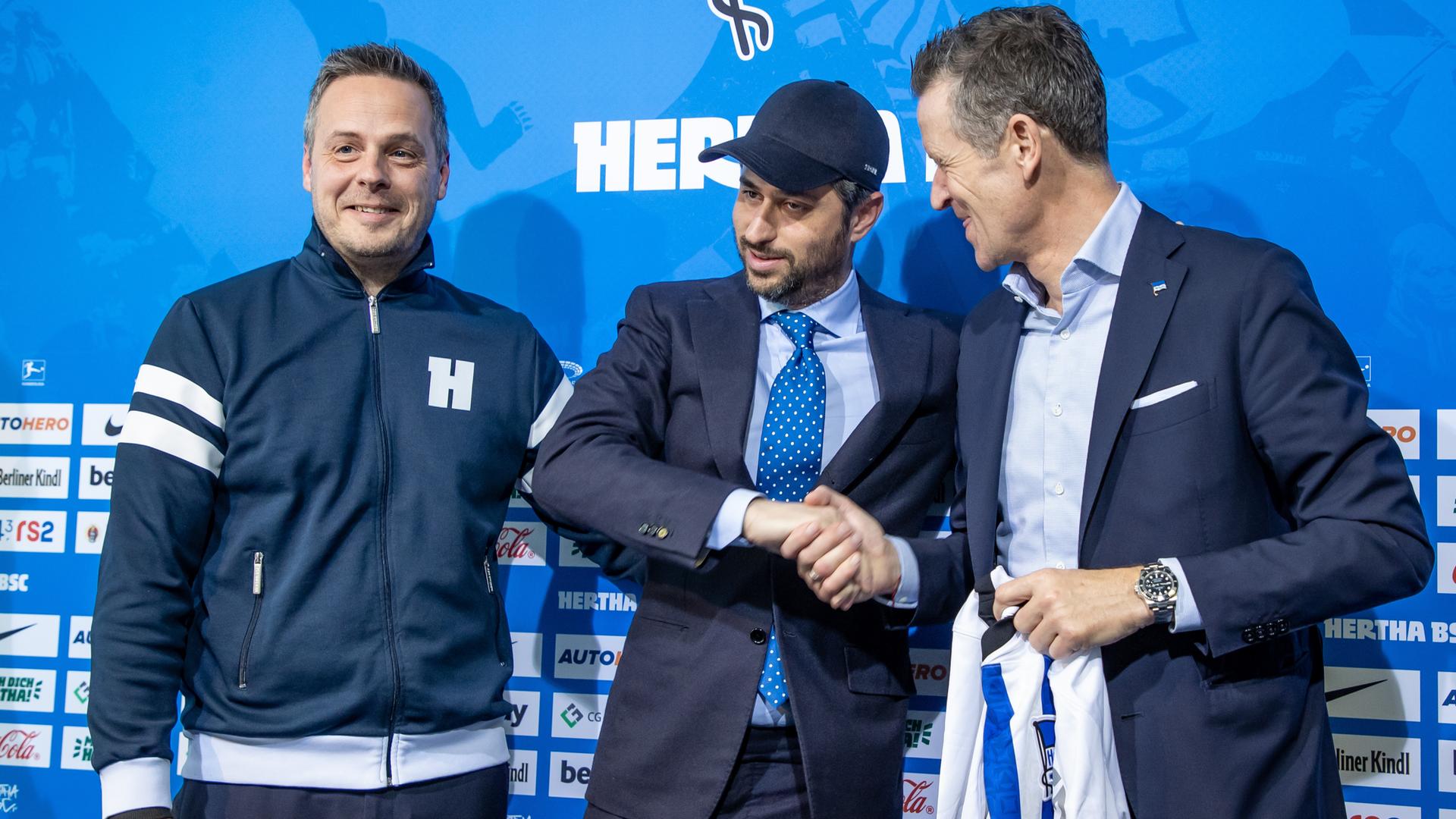 Drei Männer stehen vor dem Banner des Fußball-Bundesligisten Hertha BSC, zwei geben sich die Hand. Drei Männer stehen vor dem Banner des Fußball-Bundesligisten Hertha BSC, zwei geben sich die Hand.