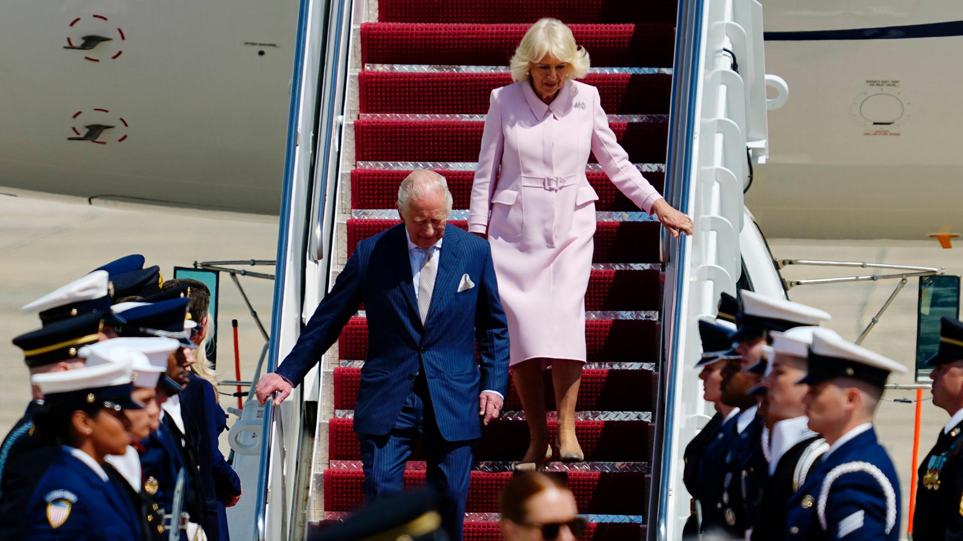 Das Foto zeigt den britischen König Charles und Königin Camilla, die aus dem Flugzeug steigen. Sie sind zu einem Staatsbesuch in den USA eingetroffen und werden von Militärs empfangen. 