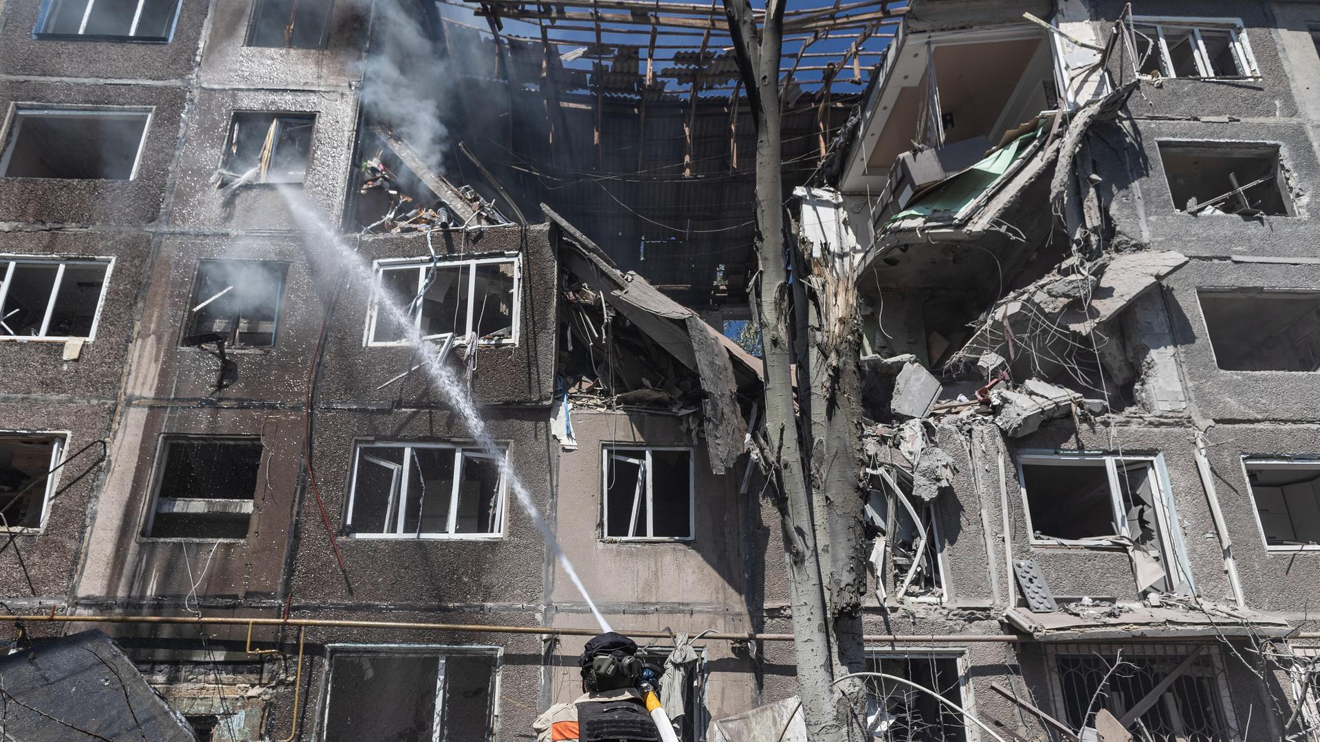 In der ukrainischen Stadt Kostiantynivka versuchen Feuerwehrleute, die Folgen eines russischen Bombenangriffss zu bekämpfen. Sie stehen mit Löschschläuchen vor einem zerstörten Wohnhaus.