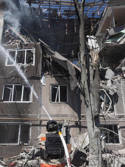 In der ukrainischen Stadt Kostiantynivka versuchen Feuerwehrleute, die Folgen eines russischen Bombenangriffss zu bekämpfen. Sie stehen mit Löschschläuchen vor einem zerstörten Wohnhaus.