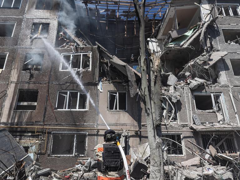 In der ukrainischen Stadt Kostiantynivka versuchen Feuerwehrleute, die Folgen eines russischen Bombenangriffss zu bekämpfen. Sie stehen mit Löschschläuchen vor einem zerstörten Wohnhaus.