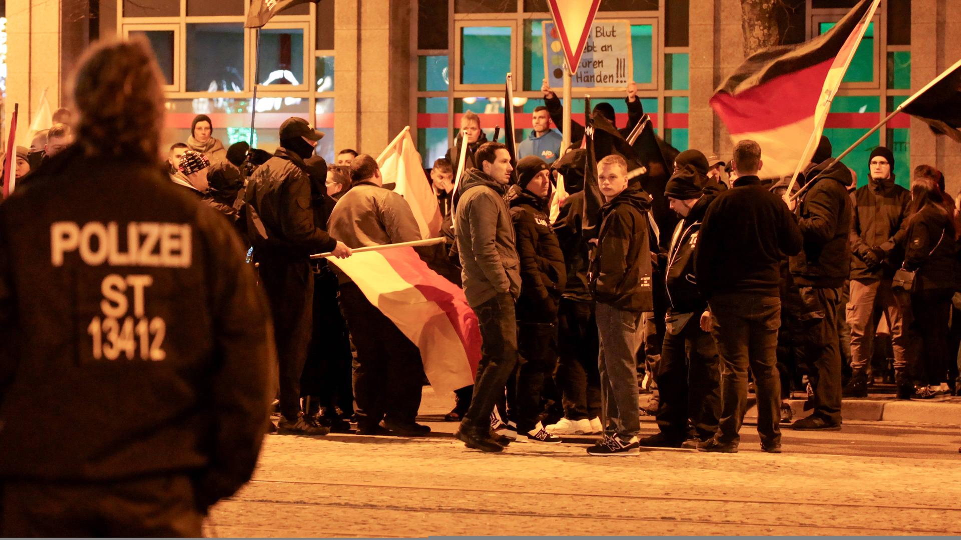 Eine Polizistin blickt auf eine Gruppe von Menschen, die überwiegend dunkel gekleidet sind.