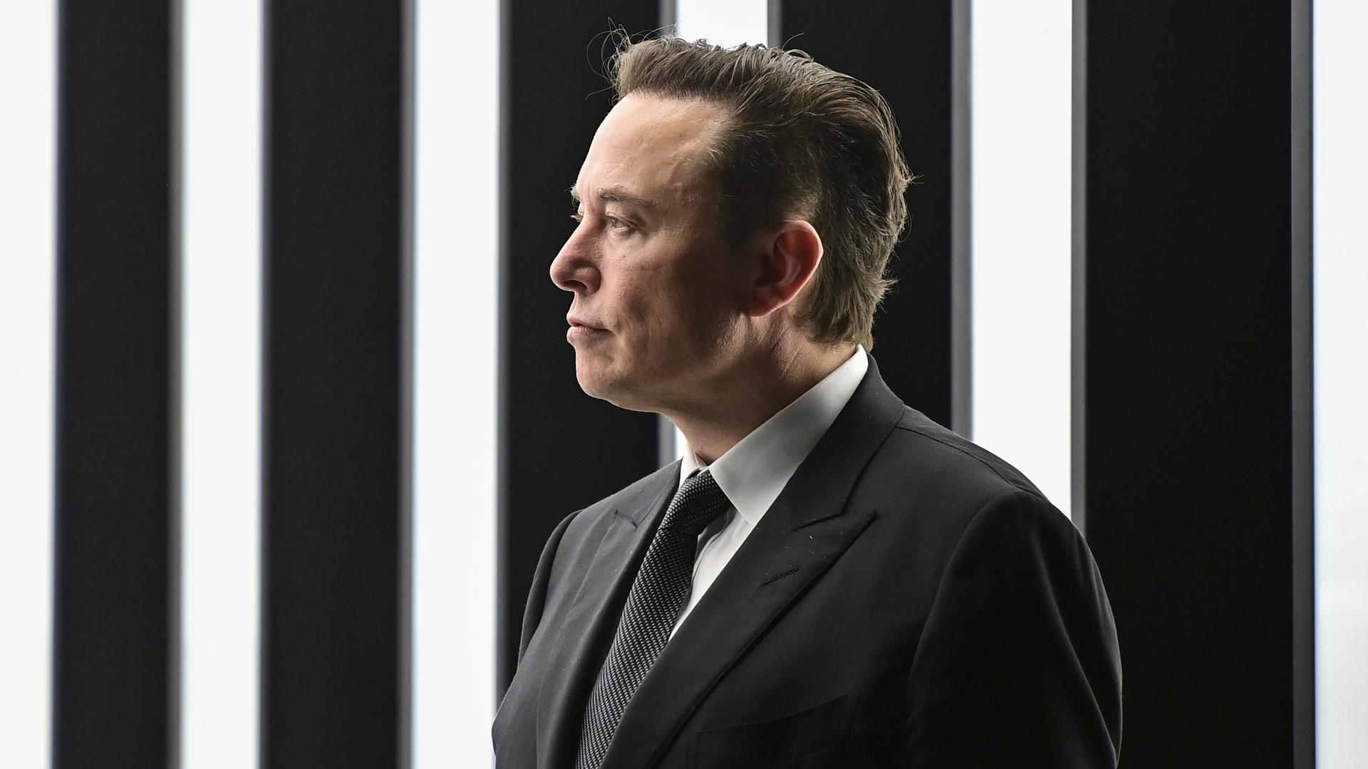 Tech-Milliardär Elon Musk im schwarzen Anzug vor schwarz-weißem Hintergrund. 