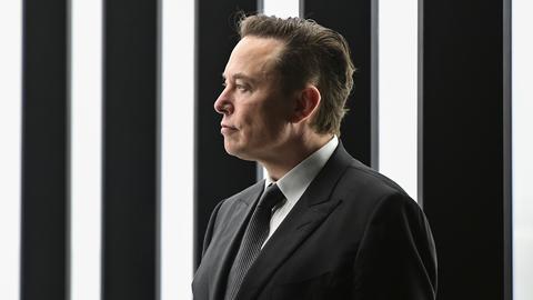 Tech-Milliardär Elon Musk im schwarzen Anzug vor schwarz-weißem Hintergrund. 