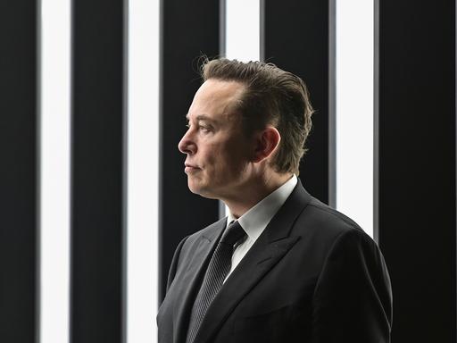 Tech-Milliardär Elon Musk im schwarzen Anzug vor schwarz-weißem Hintergrund. 