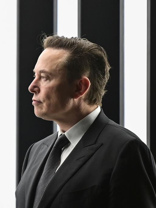 Tech-Milliardär Elon Musk im schwarzen Anzug vor schwarz-weißem Hintergrund. 