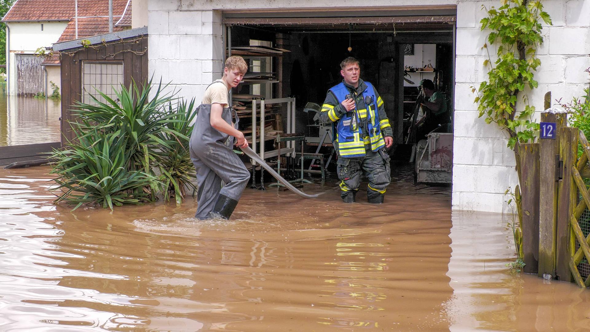 Einsatzkräfte in der Region Blieskastel im Saarland stehen mit Gummistiefeln im Wasser vor einem Haus.