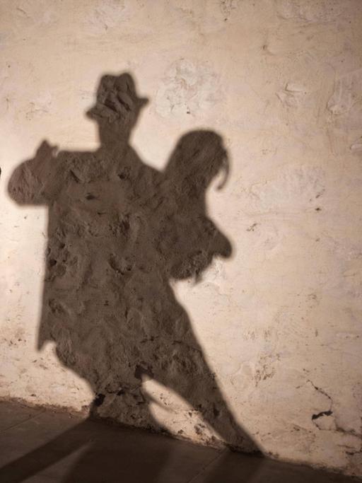 Ein tanzendes Tangopaar wirft seine Schatten auf eine grobe Wand.