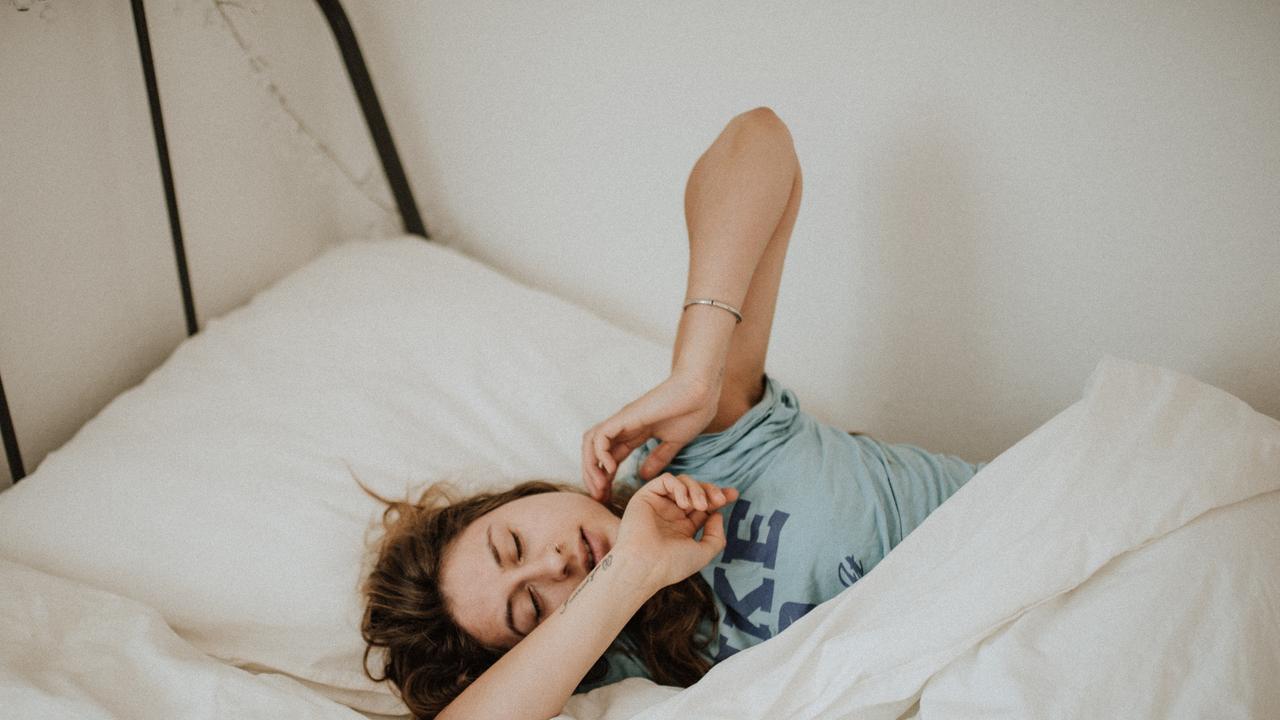 Das Bild zeigt eine Frau, die sich nach dem Aufwachen im Bett streckt. 