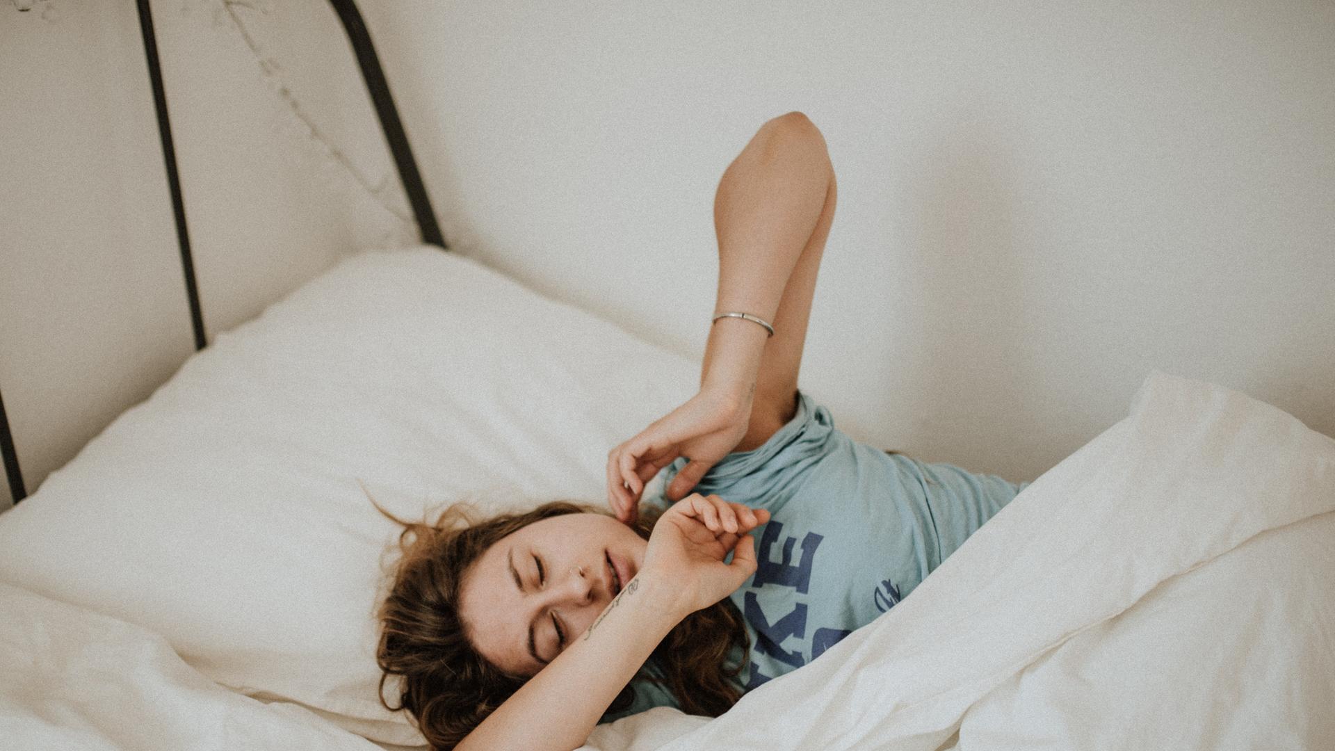 Das Bild zeigt eine Frau, die sich nach dem Aufwachen im Bett streckt. Das Bild zeigt eine Frau, die sich nach dem Aufwachen im Bett streckt.