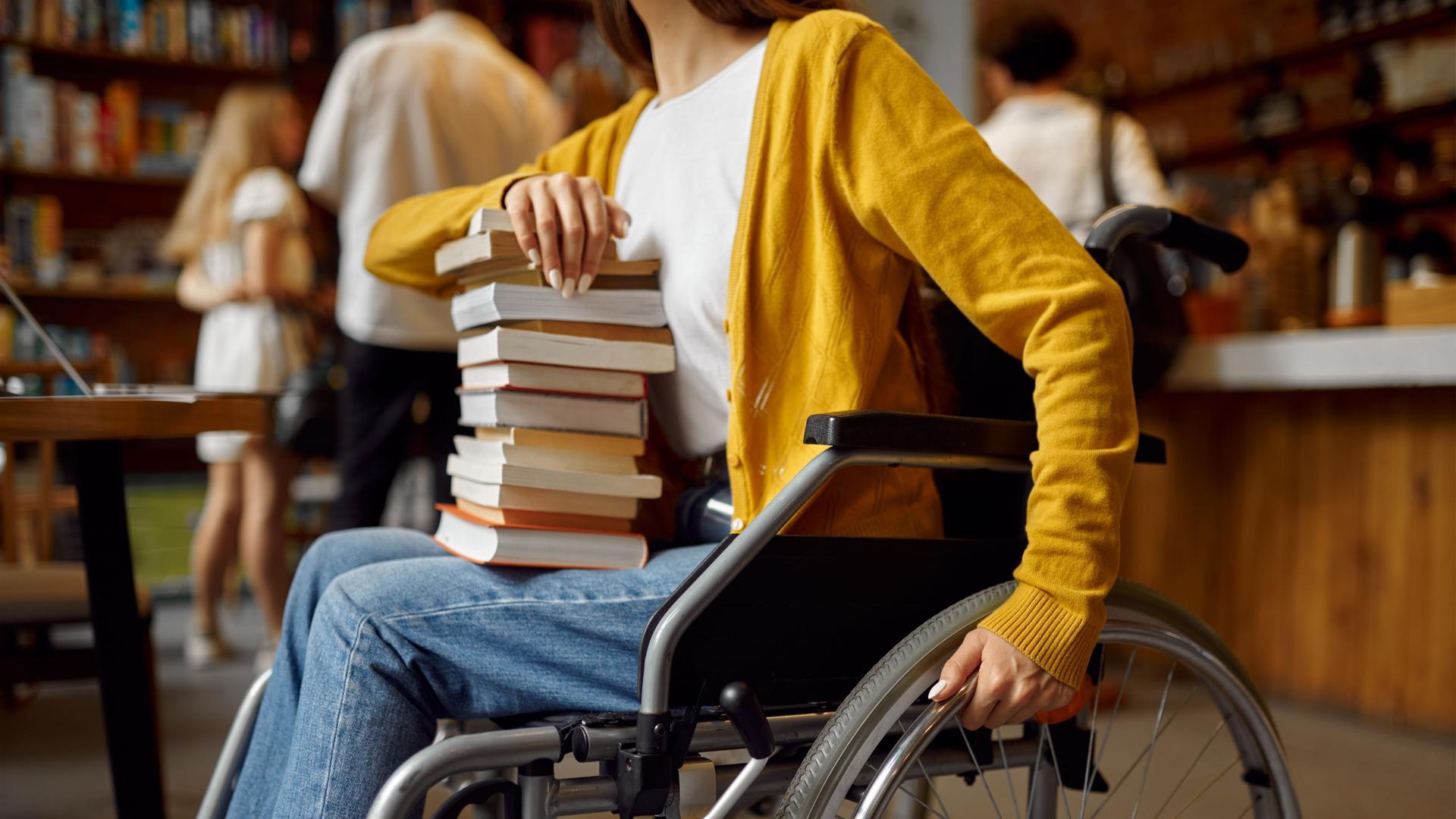 Eine Frau im Rollstuhl hält einen Stapel mit Büchern auf dem Schoß. Foto: imago Eine Frau im Rollstuhl hält einen Stapel mit Büchern auf dem Schoß. Foto: imago