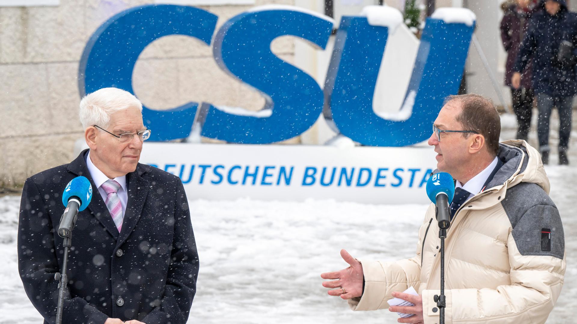 Josef Schuster und Alexander Dobrindt stehen bei winterlichem Wetter vor einem großen, blauen Logo der CSU.