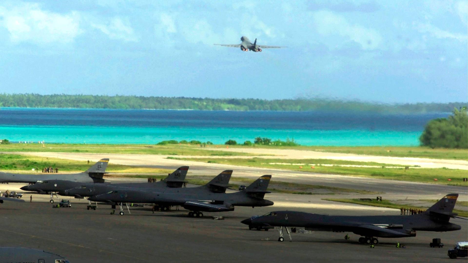 US-amerikanische Militärflugzeuge starten von einer Militärbasis aus. Im Hintergrund ist das türkisblaue Wasser der Lagune.