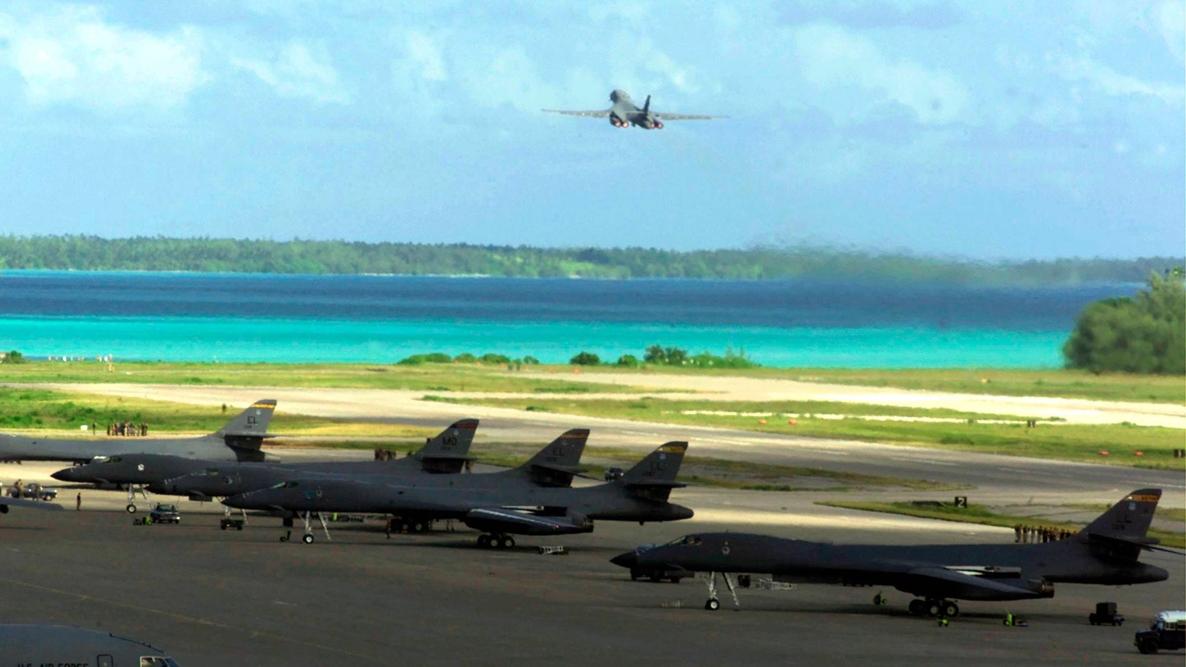 US-amerikanische Militärflugzeuge starten von einer Militärbasis aus. Im Hintergrund ist das türkisblaue Wasser der Lagune zu sehen.