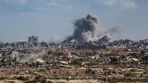 Block aus großer Ferne auf eine besiedelte Gegend im Gazastreifen. Am Horizont steigt Rauch auf. 
