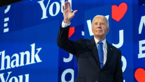 US-Präsident Biden winkt, während er von der Bühne geht. Hinter ihm Schilder an der Wand mit Herzen und den Worten "Thank you".