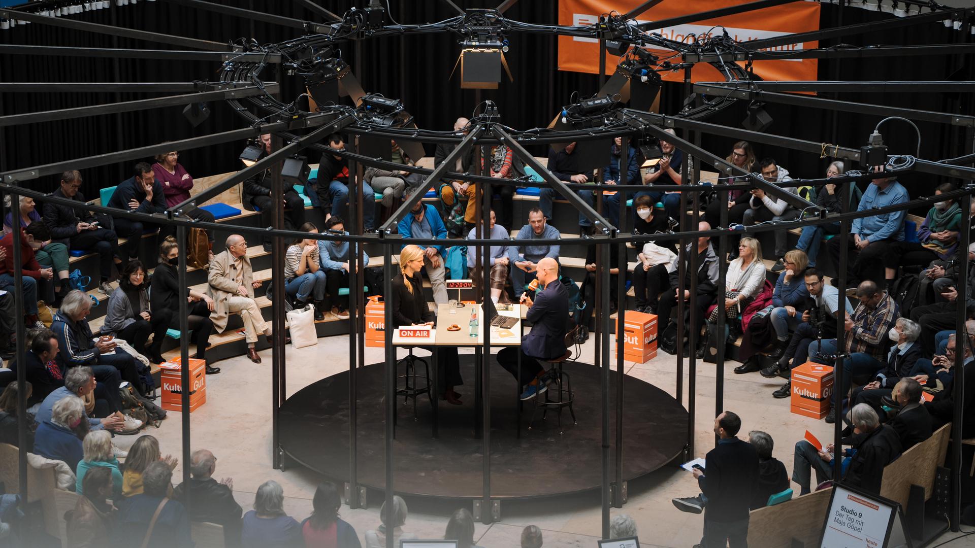 Sendungsgast Maja Göpel sitzt mit Moderator Korbinian Frenzel bei einer Livesendung in einem Rondell im Berliner Humboldt-Forum.