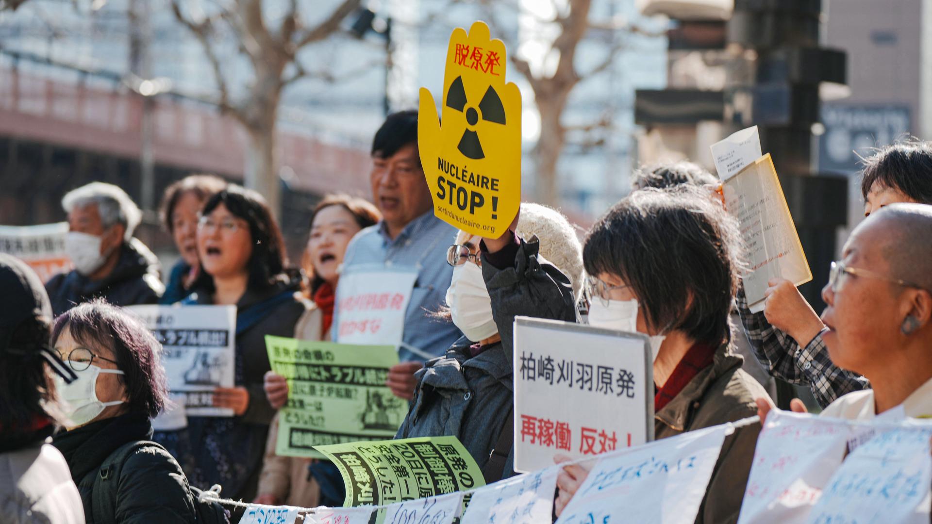 Eine Gruppe von Demonstrierenden, einige halten Banner unter anderem mit der Aufschrift "Stop Nuklear" in die Luft.