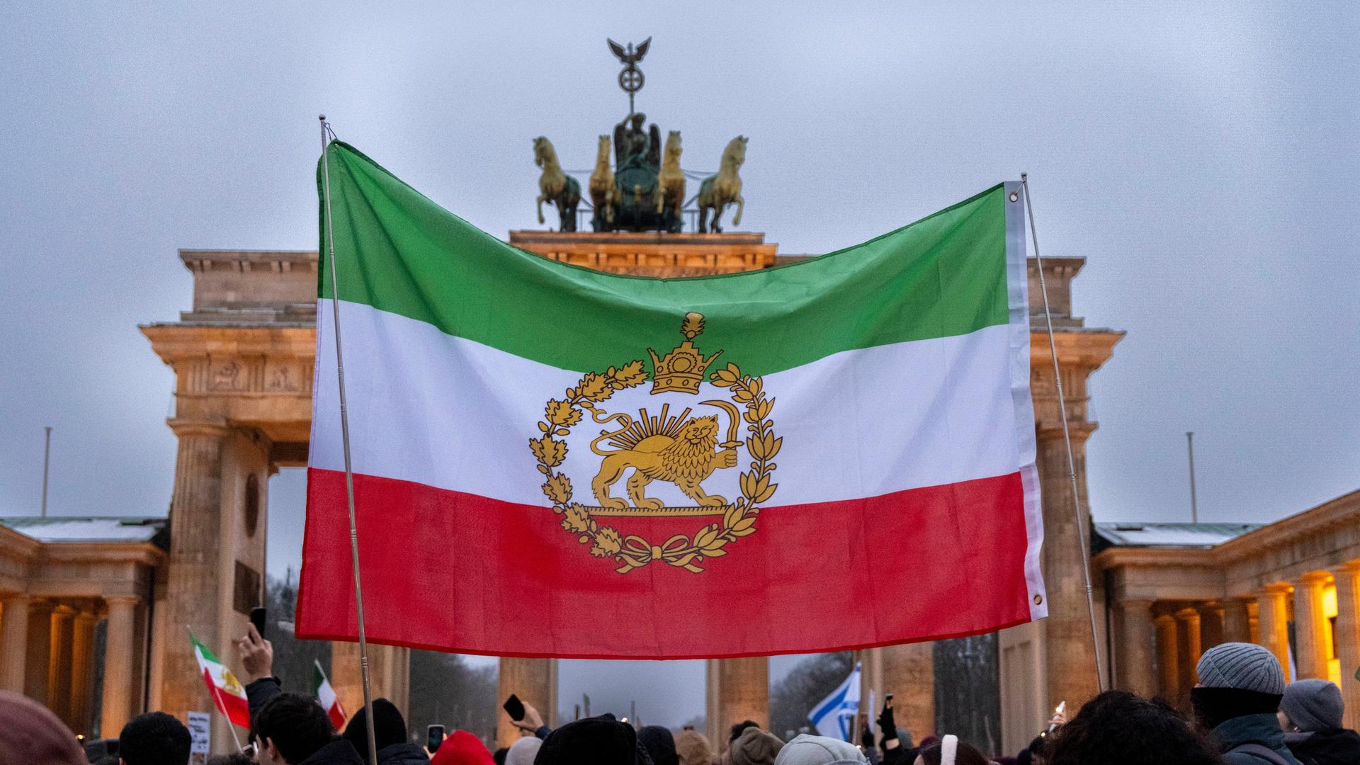 Demonstration gegen das Mullah-Regime im Iran am Brandenburger Tor in Berlin. Eine historische iranische Fahne wird vor dem Brandenburger Tor hochgehalten. 