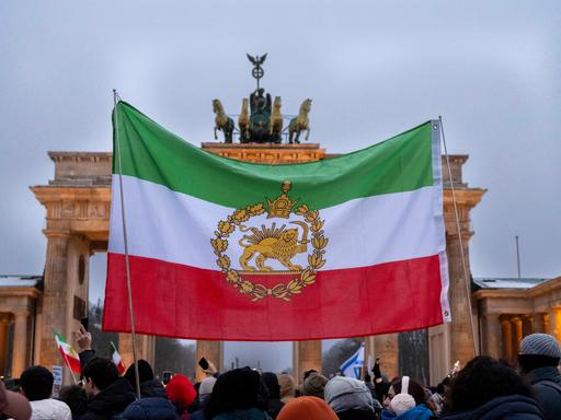 Demonstration gegen das Mullah-Regime im Iran am Brandenburger Tor in Berlin. Eine historische iranische Fahne wird vor dem Brandenburger Tor hochgehalten. 