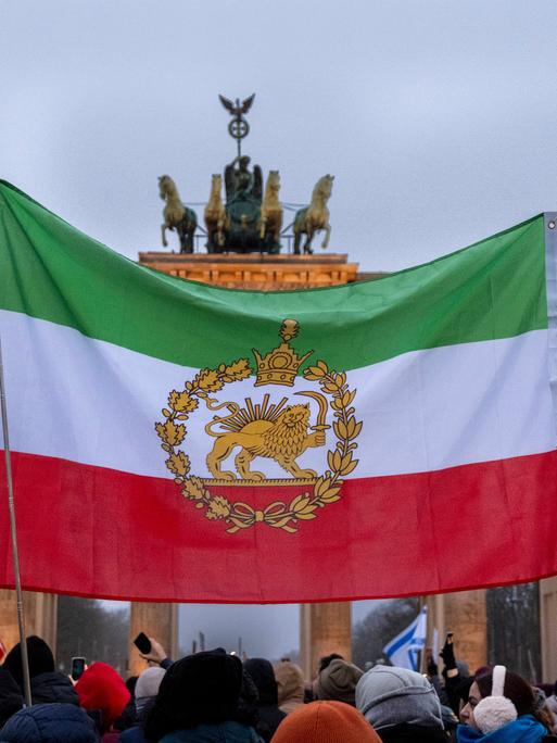 Demonstration gegen das Mullah-Regime im Iran am Brandenburger Tor in Berlin. Eine historische iranische Fahne wird vor dem Brandenburger Tor hochgehalten. 