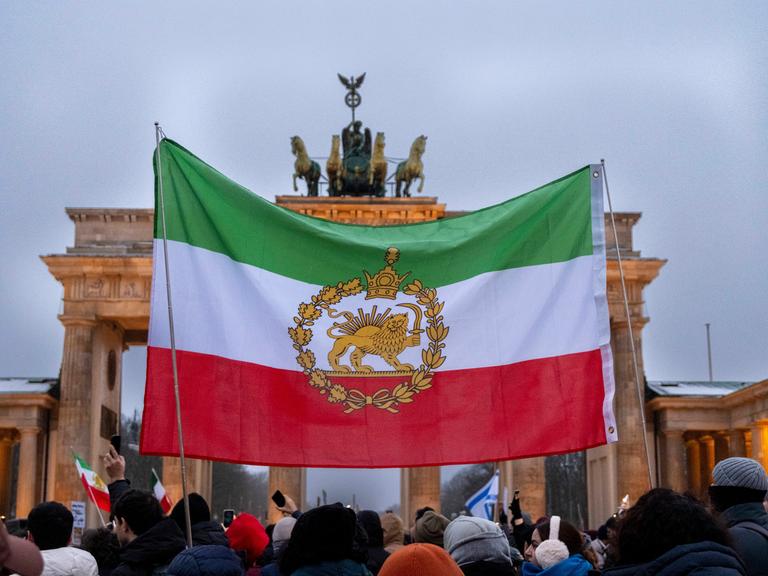 Demonstration gegen das Mullah-Regime im Iran am Brandenburger Tor in Berlin. Eine historische iranische Fahne wird vor dem Brandenburger Tor hochgehalten. 