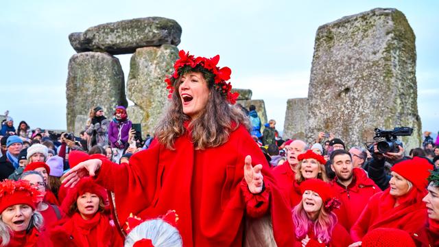 Eine große Gruppe von Menschen. Sie tragen rote Umhänge. Sie feiern vor dem Stonehenge-Stein-Kreis.