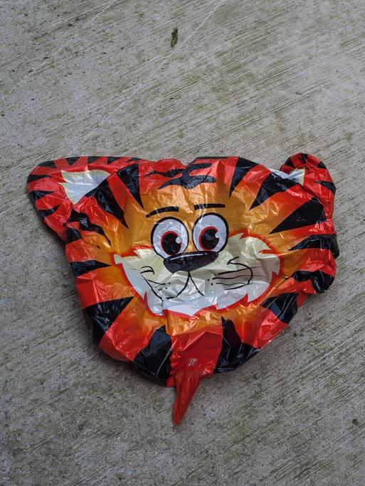 Ein leerer platter Luftballon für Kinder mit einem Tigergesicht liegt auf dem Boden.