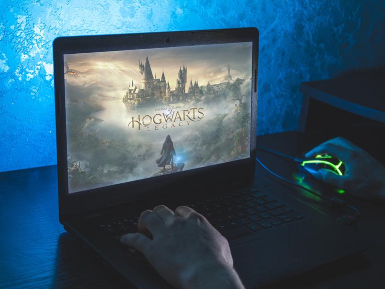 Ein Mensch sitzt vor einem Bildschirm auf dem das Spiel "Hogwarts Legacy" zu sehen ist.