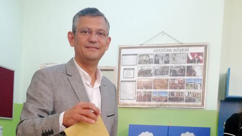 Ein älterer Mann mit Brille und grauem Anzug steckt einen braunen Briefumschlag in eine Wahlurne.