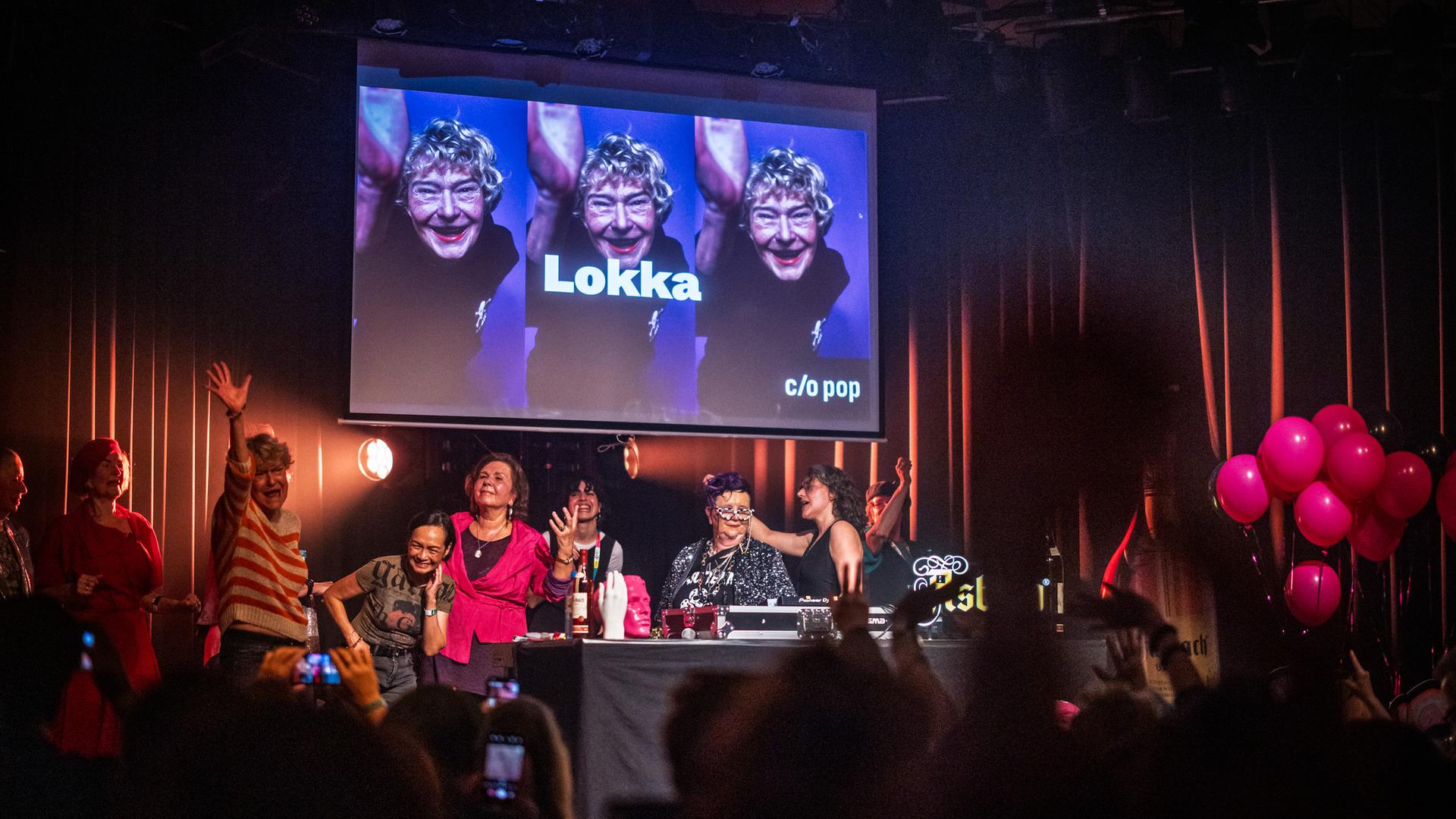 Bei einem Auftritt vor feierndem Publikum stehen mehrere ältere Frauen hinter einem DJ-Pult auf der Bühne. Bei einem Auftritt vor feierndem Publikum stehen mehrere ältere Frauen hinter einem DJ-Pult auf der Bühne.