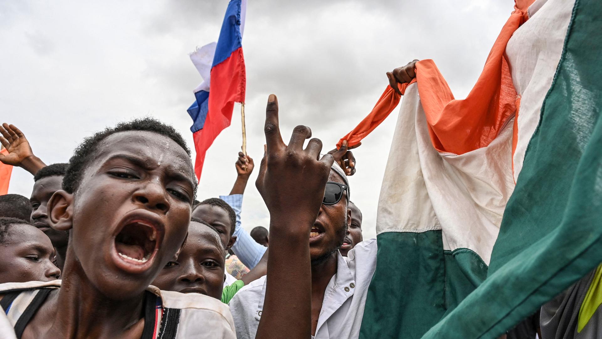 Mehrere Männer bei einer Demonstration. Sie rufen laut und schwenken nigrische Flaggen.