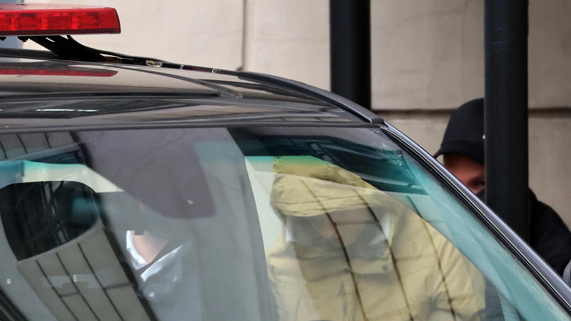"Wall Street Journal"-Reporter Evan Gershkovich erscheint zu einer Anhörung vor Gericht: Ein Mann in gelbem Anorak mit Kapuze über dem Kopf steigt mit geneigtem Kopf aus einem Polizeiauto.