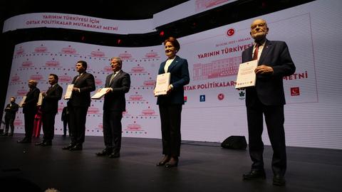 Die Vorsitzenden der Parteien stehen nebeneinander auf einer dunklen Bühne und halten jeweils das Programm in den Händen.