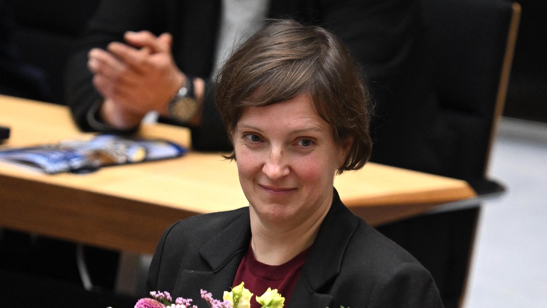 Hendrikje Klein (Die Linke) steht lächeln vor einer Abgeordnetenbank im Plenarsaal. man sieht nur ihren Kopf und die Schultern. Hinter ihr klatscht ein sitzender Abegordneter - man sieht nur seine Hände.