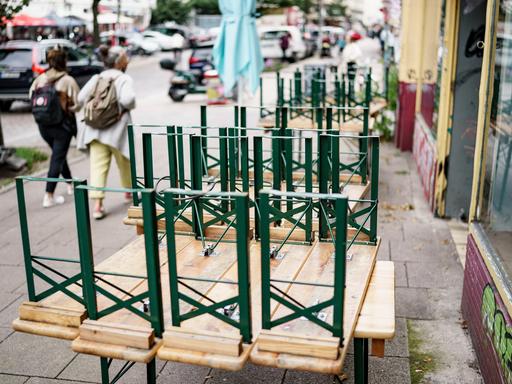 Zwei Frauen gehen im Hamburger Schanzenviertel an einem Restaurant vorbei an dem Tische vor der Eingangstür gestapelt sind.