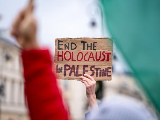 Eine Hand hält ein Schild mit der Aufschrift "Beendet den Holocaust in Palästina" bei einer Demonstration in die Höhe.