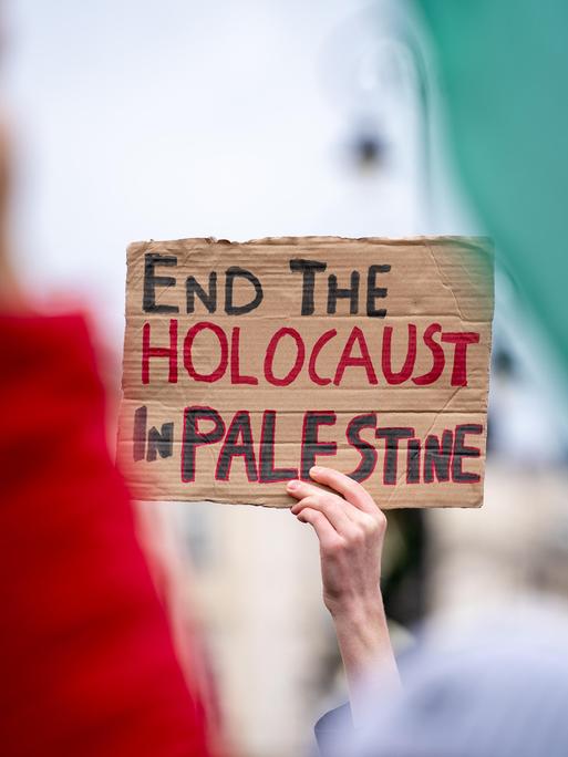 Eine Hand hält ein Schild mit der Aufschrift "Beendet den Holocaust in Palästina" bei einer Demonstration in die Höhe.