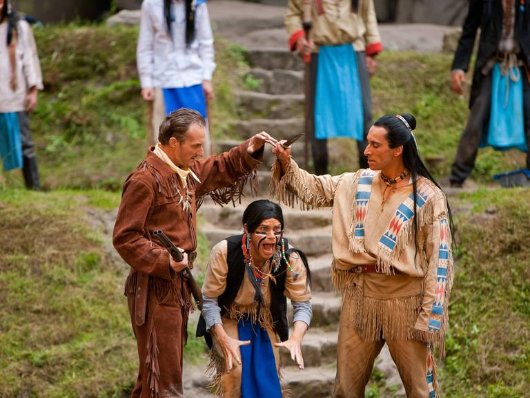 Szene aus der Karl-May-Festspiele Aufführung "Der Ölprinz". Links ein Indianer, rechts ein weisser Mann mit Gewehr.