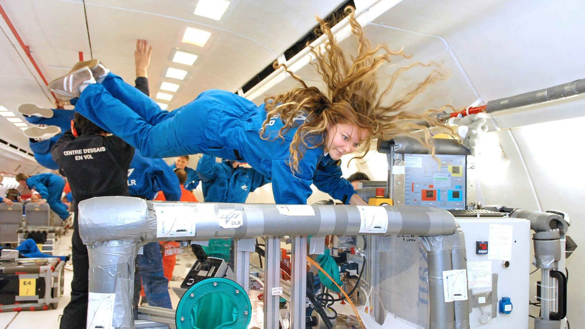 Durchführung von schwerelosen Experimenten während eines Parabelflugs. Eine Frau im blauen Overall fliegt dabei im Raum.  