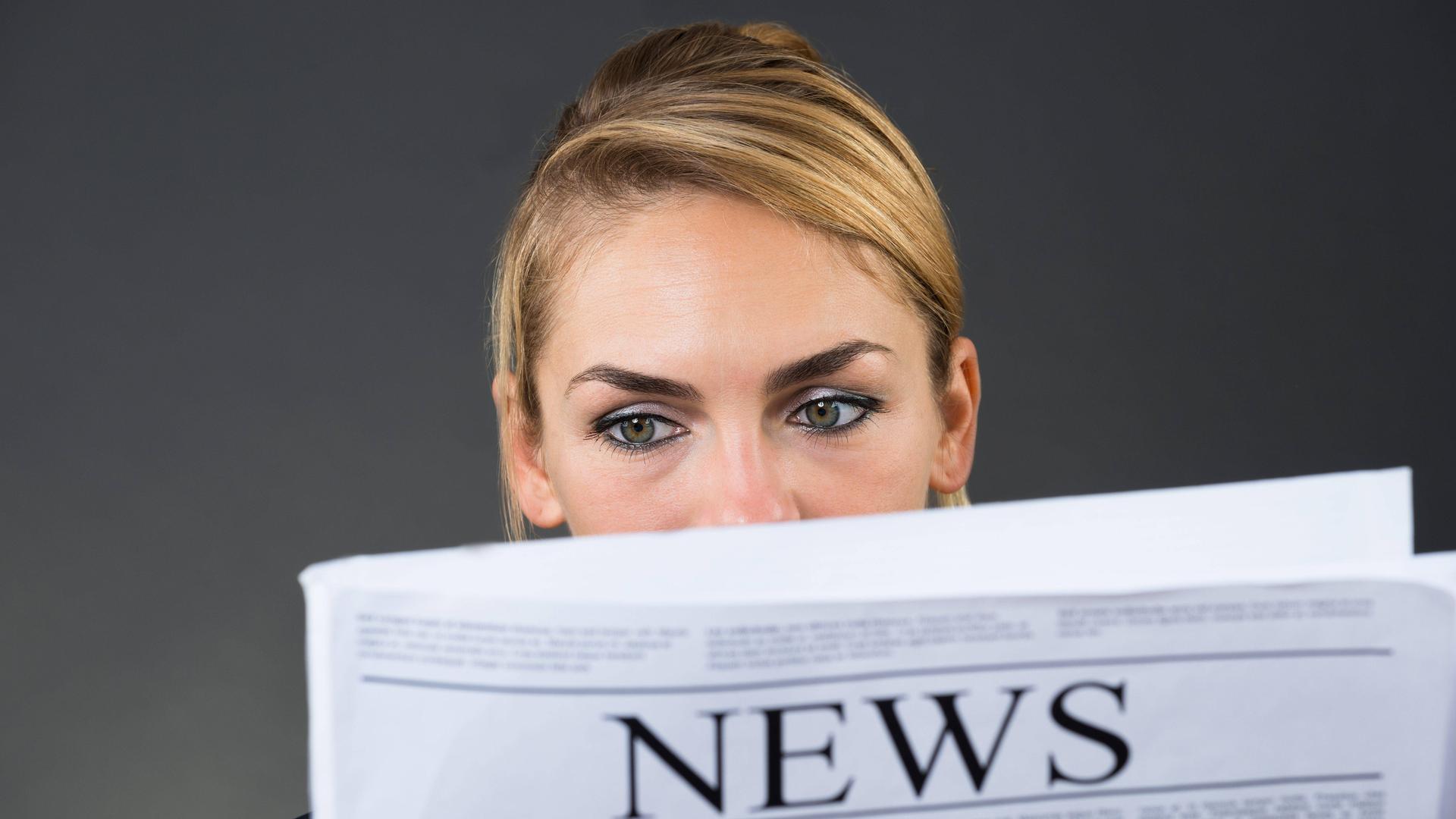 Eine junge Frau liest Zeitung auf grauem Hintergrund 